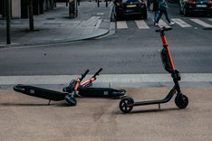 ernest-ojeh-Jmz7CfSRQzI-unsplash.jpg Zwei umgekippte E-Roller versperren den Fußweg, ein weiterer E-Roller steht daneben