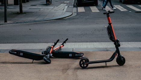 ernest-ojeh-Jmz7CfSRQzI-unsplash.jpg Zwei umgekippte E-Roller versperren den Fußweg, ein weiterer E-Roller steht daneben