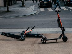 Zwei umgekippte E-Roller versperren den Fußweg, ein weiterer E-Roller steht daneben 