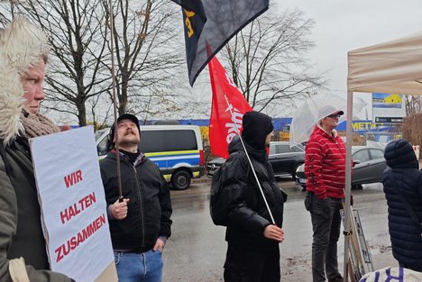 Eine Gruppe von Menschen demonstriert vor dem Dublin-Zentrum in Rahlstedt und hält Fahnen in die Luft auf denen steht: Refugees Welcome und Wir halten zusammen.