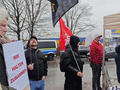 Eine Gruppe von Menschen demonstriert vor dem Dublin-Zentrum in Rahlstedt und hält Fahnen in die Luft auf denen steht: Refugees Welcome und Wir halten zusammen.