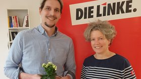 Thomas Iwan und Sabine Muhl stehen vor einem Aufsteller mit Schriftzug DIE LINKE